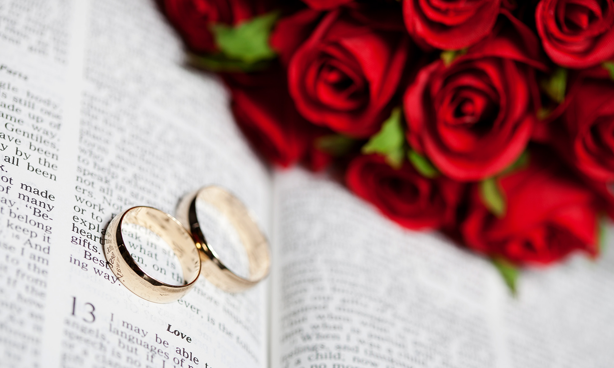 Wedding rings with Bible open at 1 Corinthians 13, with roses